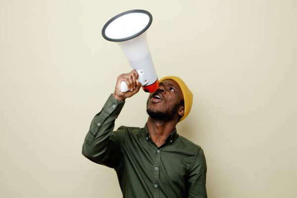 looking at up young african american male in hat wearing green shirt speaks on loudspeaker isoloated on white background